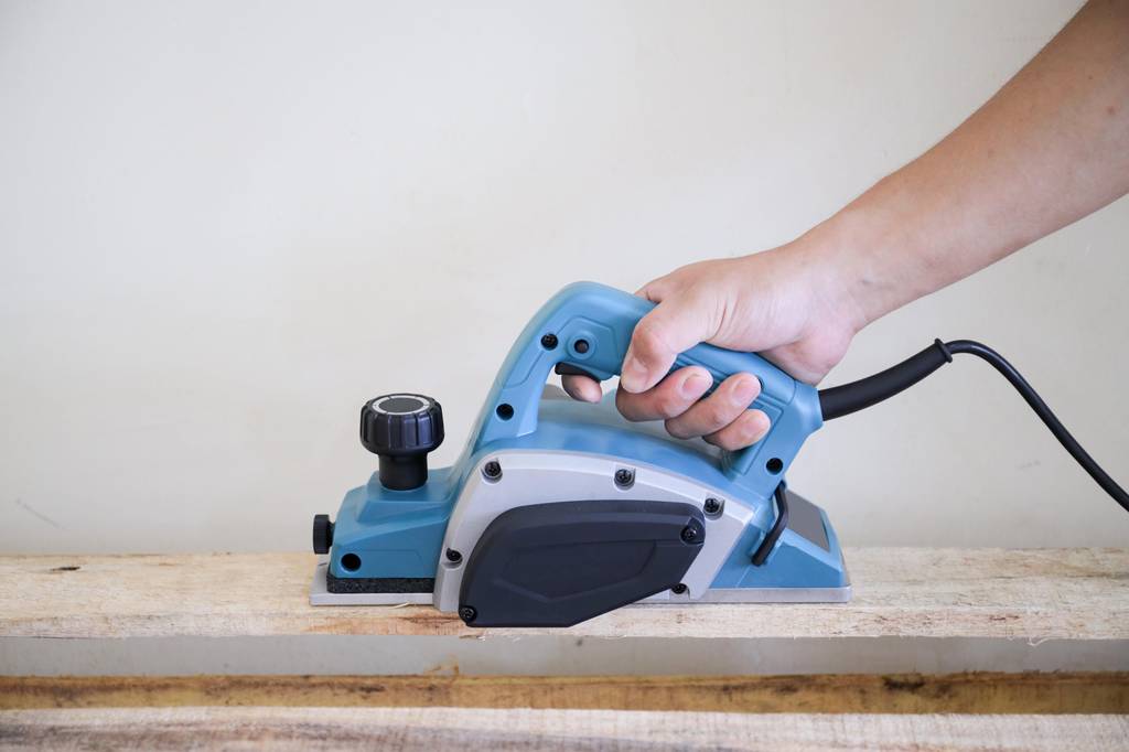 Akku-Hobel im Test: Ein blauer Elektro-Hobel mit Kabel wird auf einem sägerauem Brett geführt.