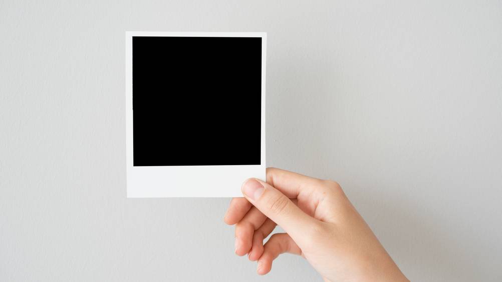 Polaroid-Kamera im Test: Ein noch unentwickeltes Polaroid-Foto in einer Hand vor weißem Hintergrund.