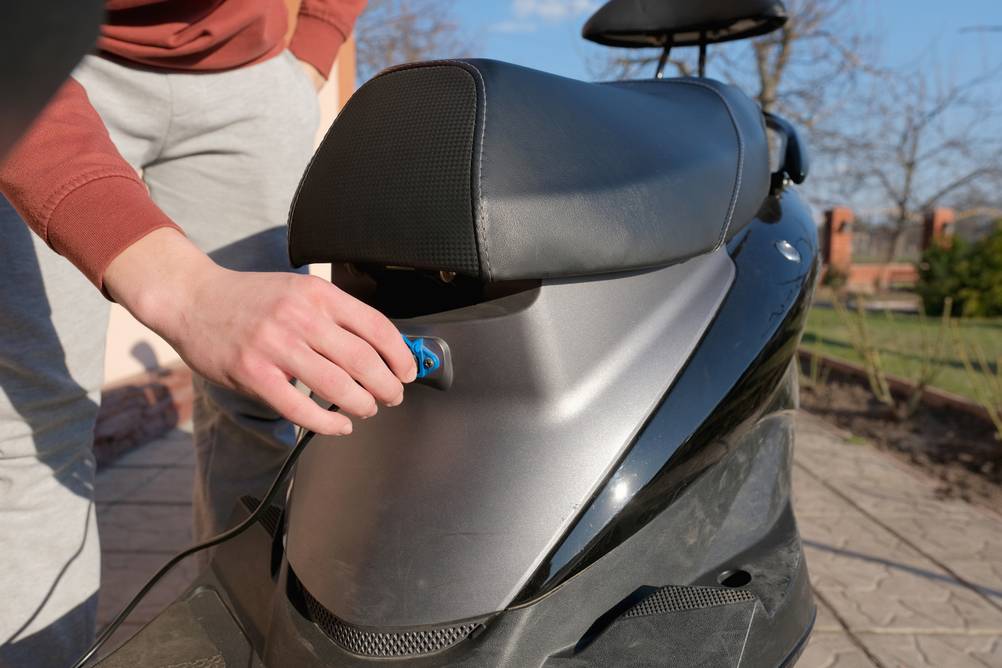 Ein junger Mann steckt ein Ladekabel in die Ladedose eines Elektrorollers, um den Akku aufzuladen.