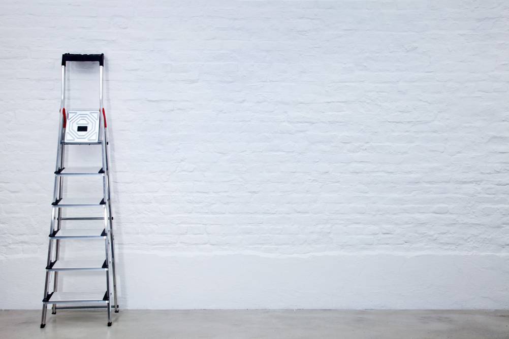 Stufenstehleiter im Test: Stufenstehleiter mit fünf Stufen und einem Podest nebst Haltebügel steht an einer Wand. 