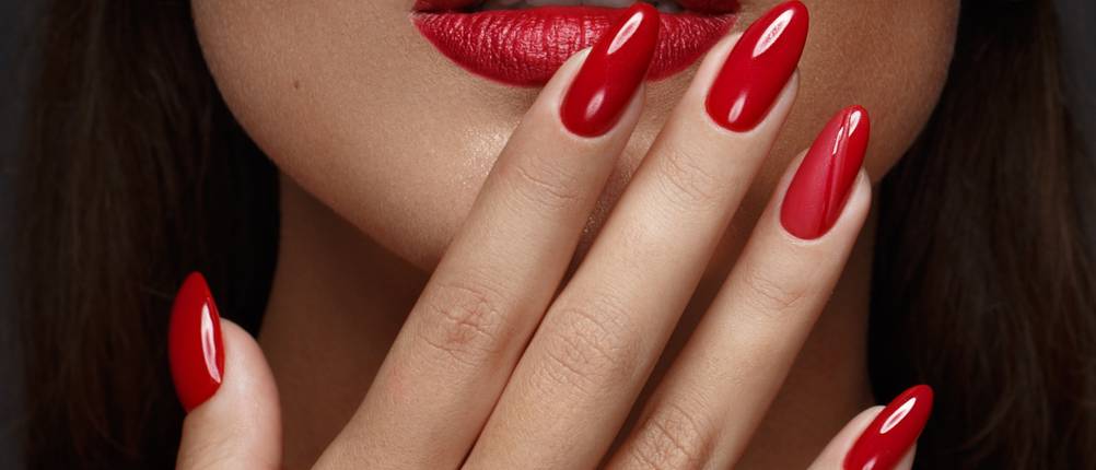 Nageldesign-Set-Test: Eine Frau hält sich die Hand mit roten Fingernägeln vor einen rot geschminkten Mund.