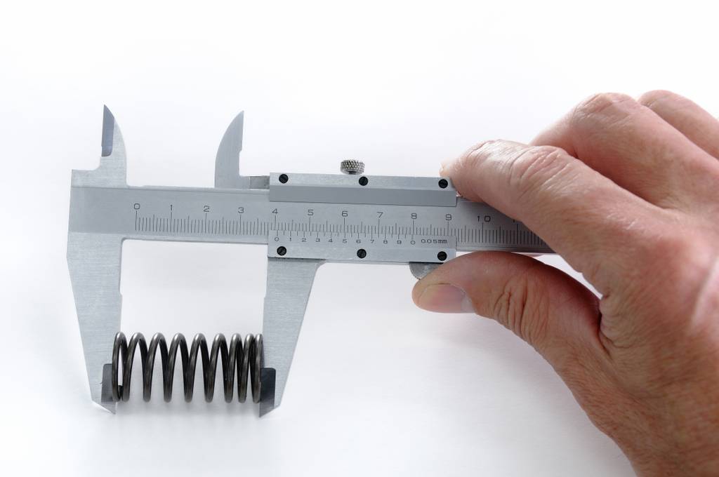 Messschieber analog im Test: Eine Feder wird von einer Hand in einem analogen Messschieber gemessen.