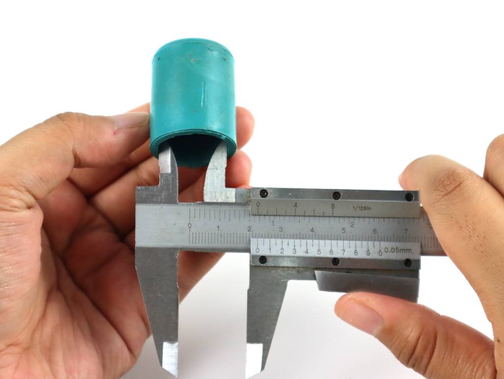 Messschieber analog im Test: der Innendurchmesser eines grünen Kunststoffteils wird gemessen – zwei Hände sind dazu zu sehen, der Hintergrund ist weiß.