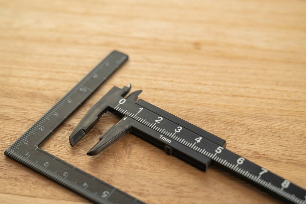 Messschieber analog im Test: Ein schwarzer analoger Messschieber und ein gleichfarbiger Messwinkel liegen auf einer Holzoberfläche
