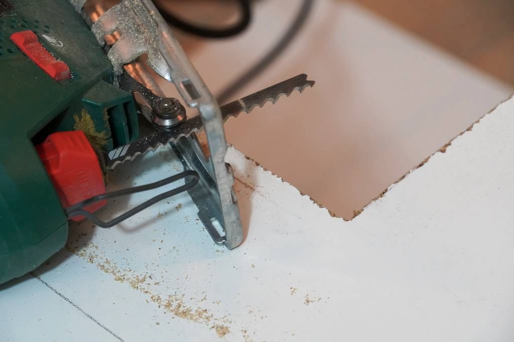 Stichsägeblatt im Test: Eine Stichsäge mit grobem Stichsägeblatt liegt auf einer geschichteten Holzplatte – ein ausgfranster Schnitt ist zu sehen.