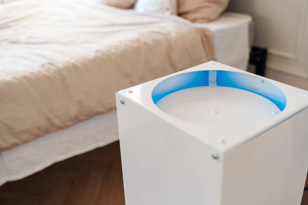 UVC-Luftreiniger im Test: Ein Gerät vor einem Bett zeigt ein blaues Licht im oberen Teil.