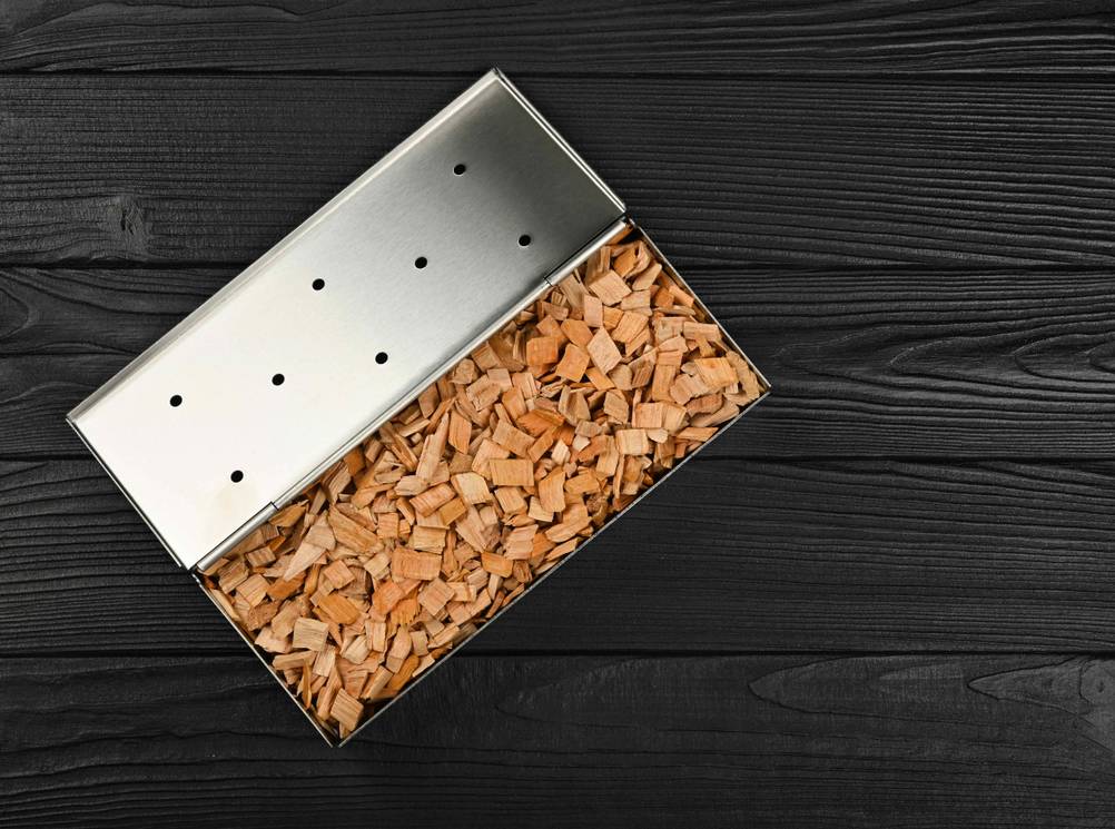 Räucherbox im Test: Gefüllte Räucherbox mit geöffnetem Deckel auf schwarzem Holz-Untergrund.