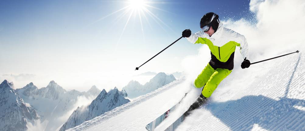 Herren-Skijacke-Test: Ein Mann fährt mit Skistecken eine Piste hinunter und hat dabei eine gelbe Skihose und Jacke an.