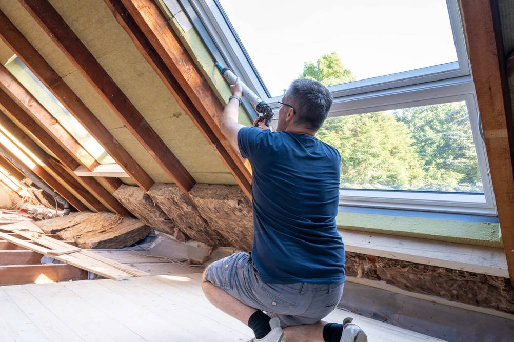 Schaumpistole im Test: Mann dichtet ein Dachfenster ab.