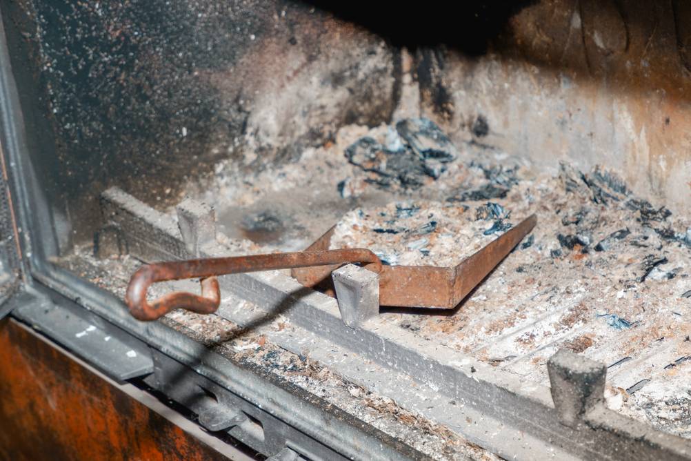 Kaminbesteck im Test: Eine rostige Schaufel in einem gröffneten Kamin mit Asche und Holzkohleresten.