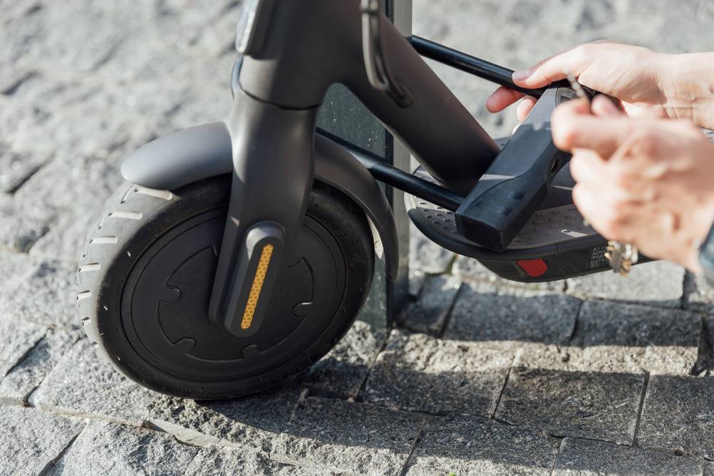 E-Scooter-Schloss getestet: Eine Hand testet ein E-Scooter-Schloss und schließt dafür ein Bügelschloss um einen E-Scooter.