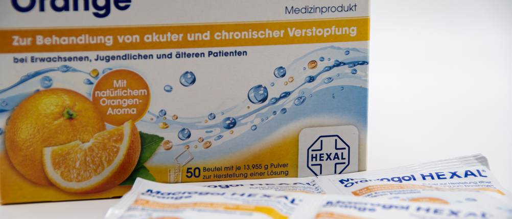 Macrogol-Test: Die Verpackung von Macrogol mit Orangengeschmack ist hinter den Beuteln aufgestellt.