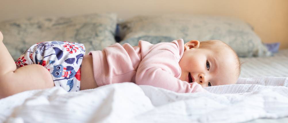 Stoffwindel-Test: Ein Baby liegt fröhlich auf einem Bett.
