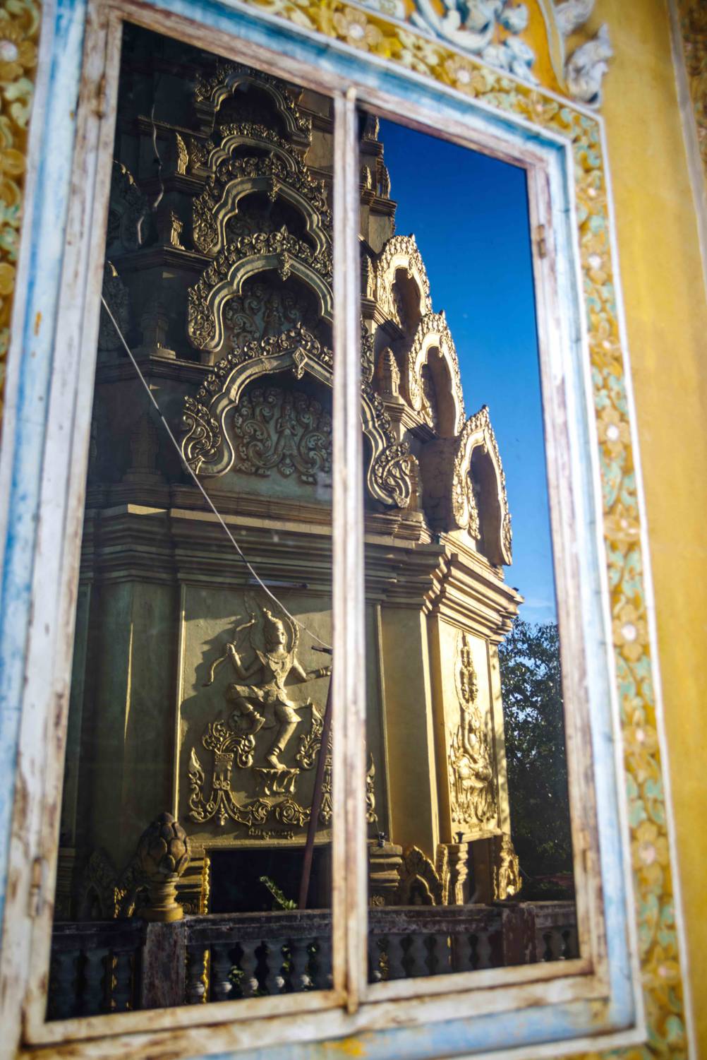 Spiegelfolie im Test: Spiegelfolie an einem reich verzierten Fenster mit Alterungsspuren – in der Scheibe ist ein asiatischer Tempel erkennbar.