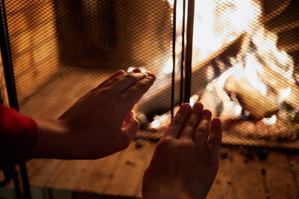 Kaminschutzgitter im Test: Kinderhände werden vor ein Kaminschutzgitter und das dahinter brennende Feuer gehalten