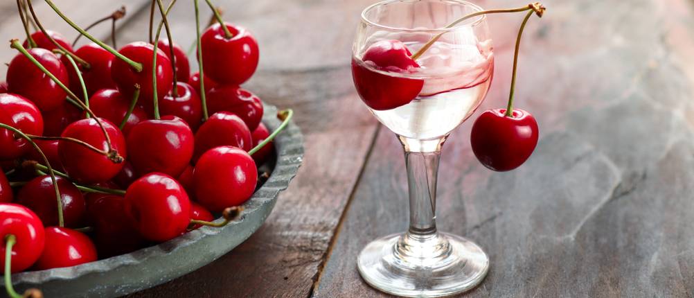 Ein Glas Likör mit einer Kirschen und eine Schale Kirschen daneben