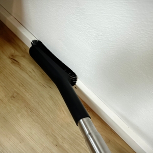 Die schmale Düse des AEG AB61H6SW Staubsaugers reinigt entlang einer weißen Fußleiste auf Parkettboden. Der Bürstenrand ist deutlich sichtbar.