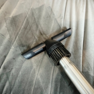 Die Polsterdüse des AEG AB61H6SW Staubsaugers gleitet über ein graues Sofa. Die Fläche zeigt sichtbare Reinigungsspuren.