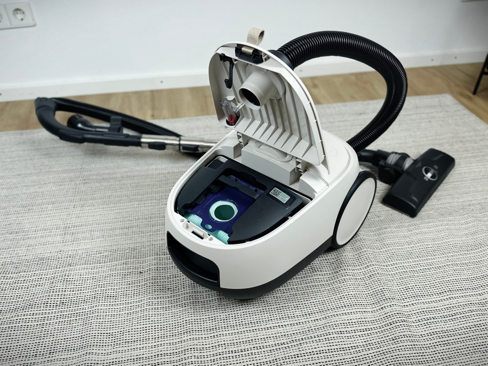 Der geöffnete Staubbeutelbehälter des AEG AB61H6SW zeigt den eingesetzten Staubbeutel. Der Deckel ist vollständig geöffnet.