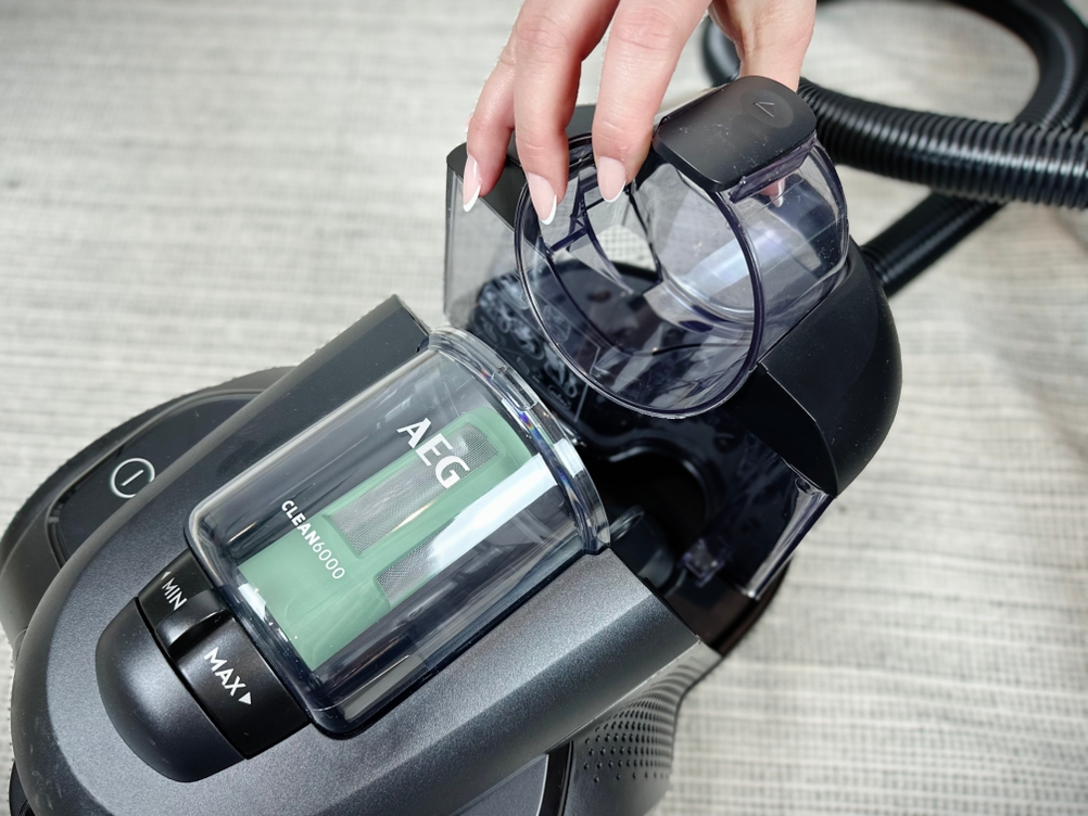 Oberseite des AEG beim Entnehmen des Staubbehälters. Eine Hand hebt den transparenten Behälter an.