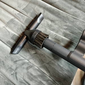 Die Polsterdüse des AEG Clean 6000 ÖKO liegt auf einem gepolsterten Stuhl. Die Bürste ist rund und hat Borsten.