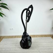 Der AEG Clean 6000 ÖKO steht einsatzbereit auf einem Teppich. Der Saugschlauch ist aufrecht eingehängt.