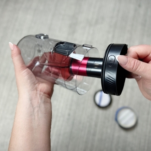 Eine Person hält den herausgenommenen Staubbehälter des AEG AP81AB25UG in der Hand und öffnet ihn an der Unterseite.