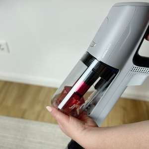 Eine Hand hält den AEG-AP81AB25UG-Staubbehälter. Die Zyklontechnik und ein Sichtfenster auf den Füllstand sind erkennbar.