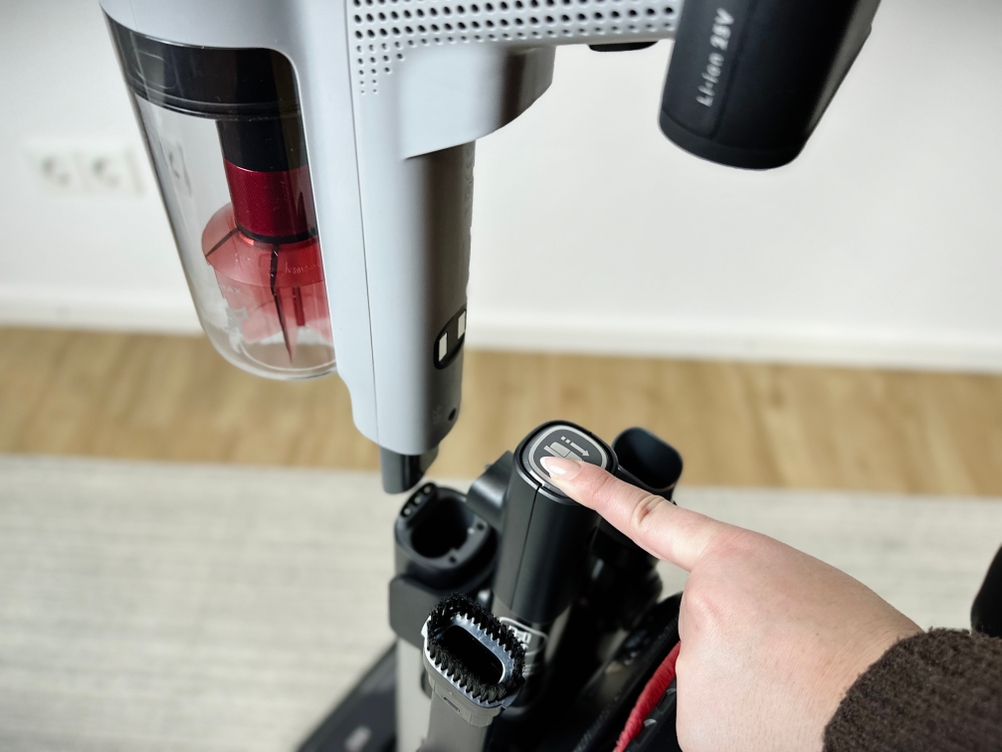 Eine Person drückt auf den Knopf zur Entriegelung eines Zubehörteils am AEG-AP81AB25UG-Staubsauger.