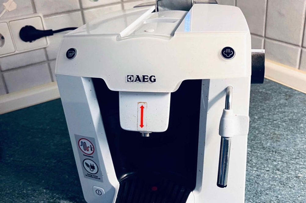 Kaffeemaschine im Test: Vorderansicht einer weißen AEG-Kaffeemaschine. Sie steht auf einem blauen Untergrund vor weißen Kacheln.
