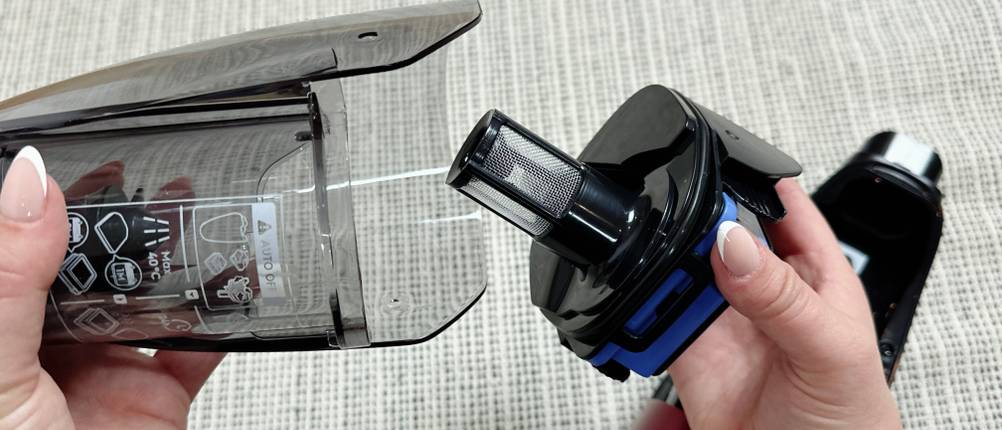 Der Staubbehälter des AEG QX7-1ULTAN wird geöffnet, während eine Person den Filter entnimmt.