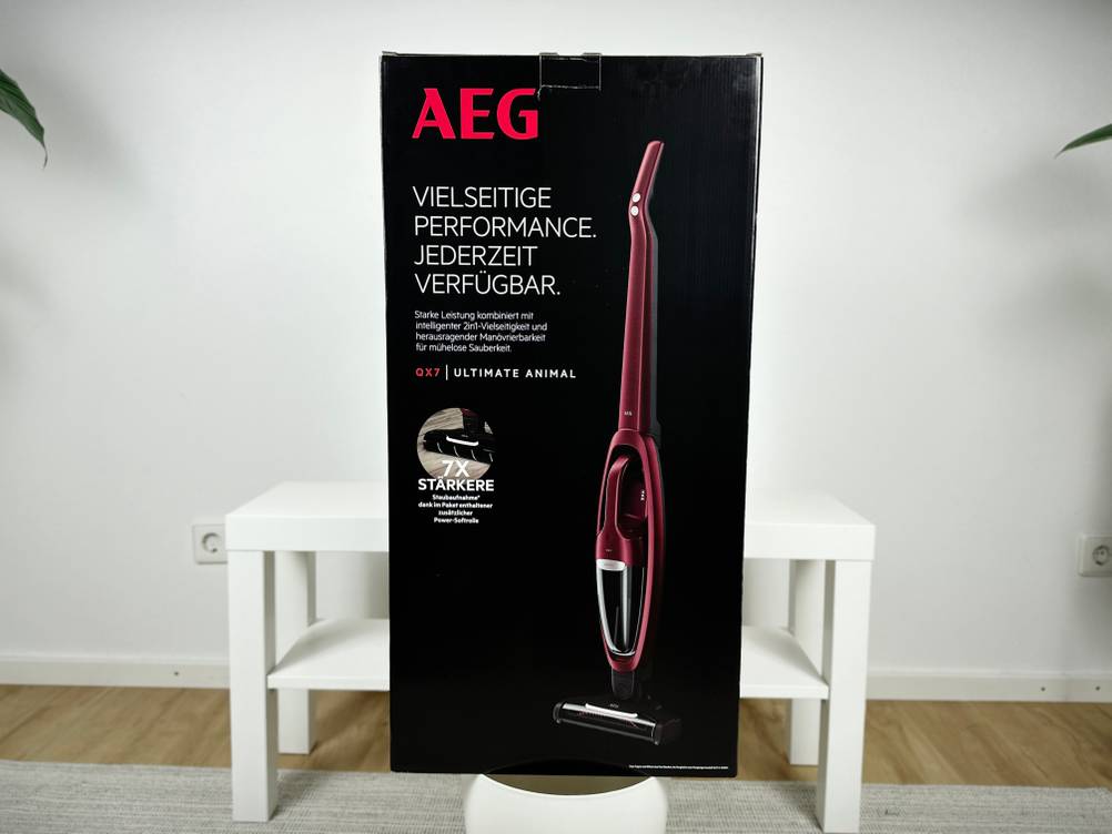 Die Verpackung des AEG QX7-1ULTAN Akkustaubsaugers steht vor einem weißen Hintergrund. Das Design zeigt das Gerät sowie wesentliche Produktmerkmale und Leistungsversprechen.
