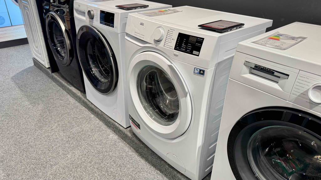 Eine AEG-Waschmaschine 7 kg steht zwischen anderen Marken zum testen in einem großen Raum.