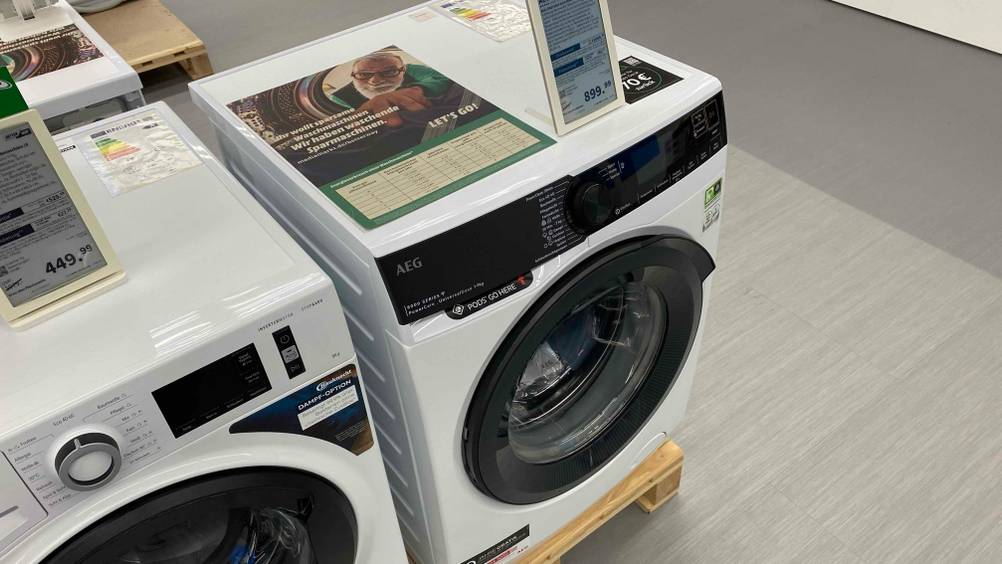 Im Test: Eine AEG-Waschmaschine von schräg oben auf einem Holzsockel neben anderen Geräten.