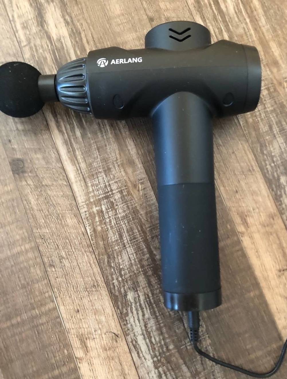 Schwarze kabelgebundene Aerlang Massagepistole im Test liegt auf einer Holzfläche.
