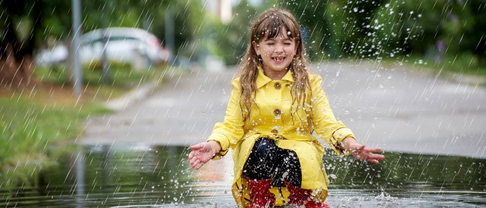 Aigle-Gummistiefel-Test: Kind in gelber Regenjacke und roten Gummistiefeln spielt in einer Regenpfütze.