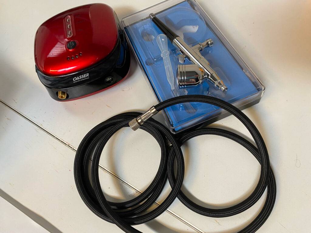 Airbrush-Set im Test: Der Anschlussschlauch liegt mit dem Set auf einer weißen Fläche.