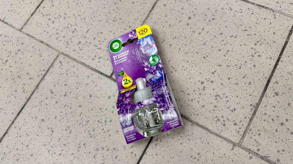 Ein getesteter Duftstecker in der Verpackung liegt auf einem Fliesenboden.