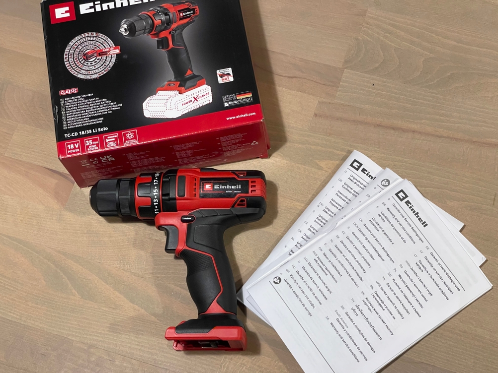 Einhell Akku-Bohrschrauber mit Verpackung und mehrsprachiger Bedienungsanleitung auf hellem Holzuntergrund.