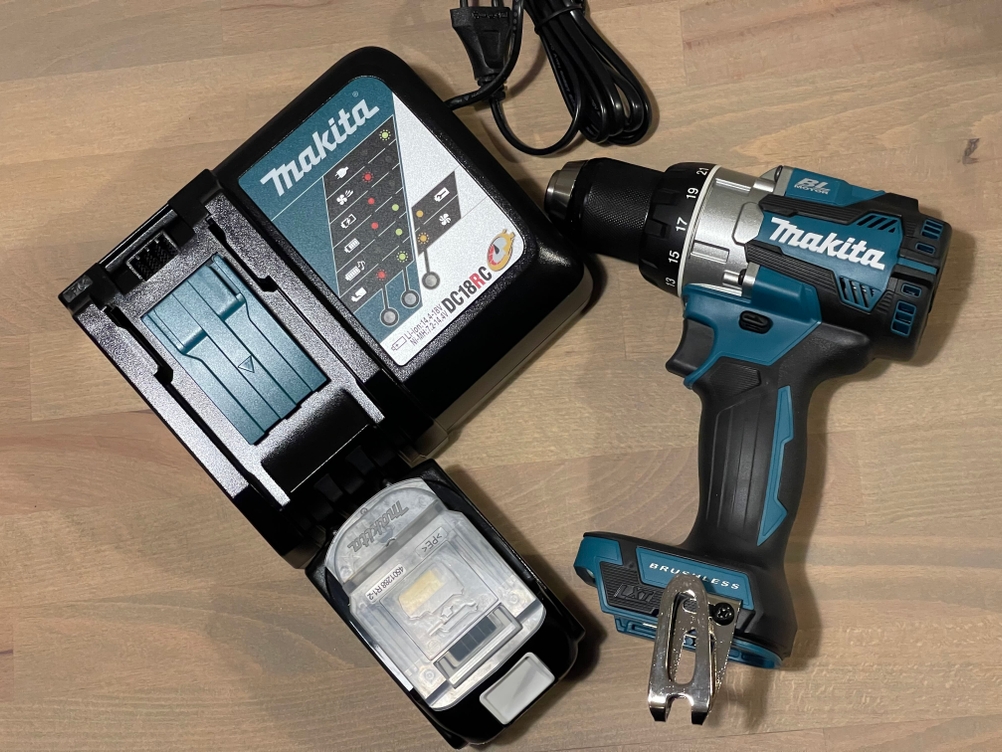 Makita Akku-Bohrschrauber neben dem zugehörigen Ladegerät auf einem Holztisch liegend.