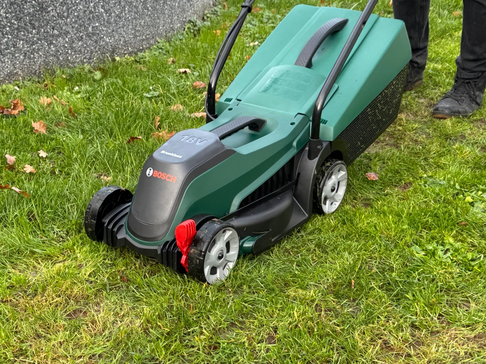 Der getestete Akku-Rasenmäher von Bosch steht auf einem Rasen.