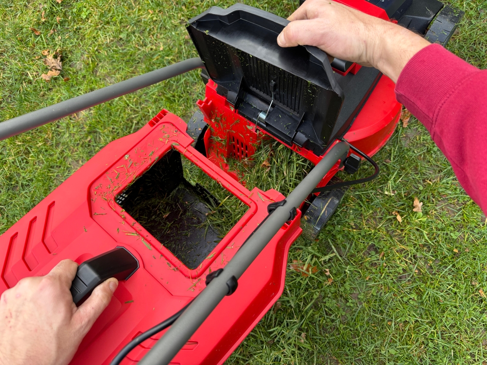 Eine Person entnimmt den vollen Fangkorb beim getesteten Akku-Rasenmäher von Einhell.