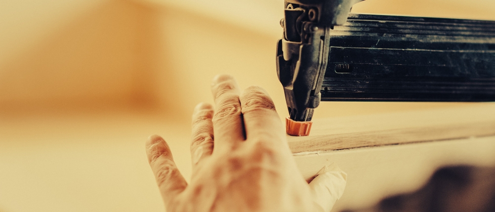 Ein Nutzer tackert mit einem Akku-Tacker eine Holzleiste. Die Hand hält das Werkstück ruhig fest, während das Gerät angesetzt wird.