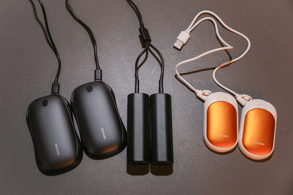 Taschenwärmer getestet: Drei elektrische Taschenwärmer und die jeweiligen Ladekabel liegen auf einem Tisch.