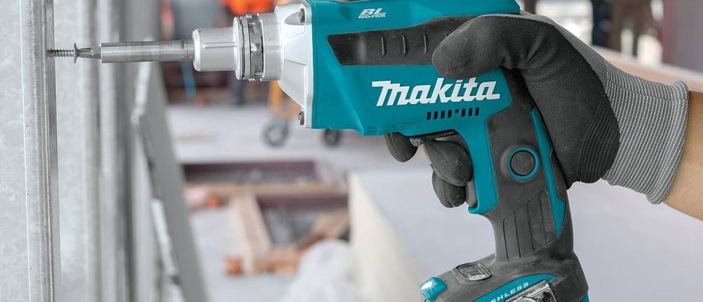 Akku-Trockenbauschrauber-Test: Eine Hand mit Handschuh hält ein Makitagerät mit Bit und Schraube an ein Trockenbaugestell auf einer Baustelle.