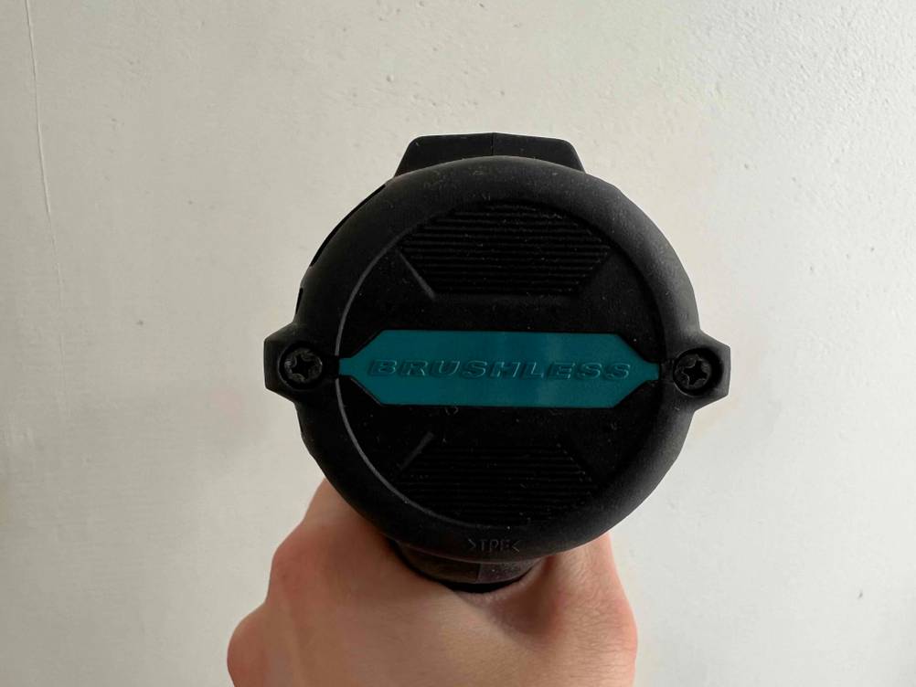 Eine Hand hält einen Akkuschrauber bürstenlos mit der Rückseite vor eine helle Wand.