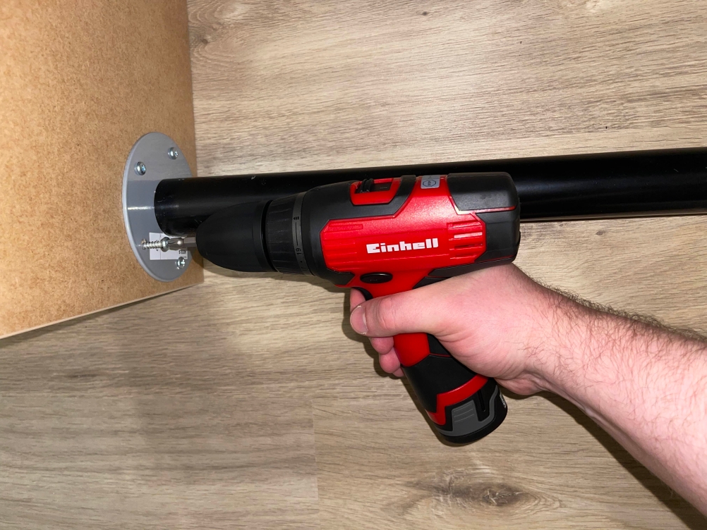 Einhell TH-CD 12-2 Li Akkuschrauber in rot mit schwarzem Griff wird von einer Hand über einer hellen Holzfläche gehalten.