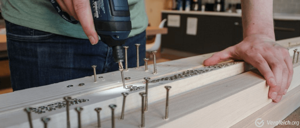Ein Akkuschrauber dreht eine Schraube in eine Holzplanke.