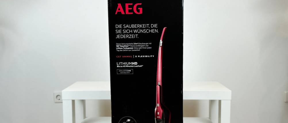 Die Verpackung des AEG Ergorapido CX7-2-45AN zeigt den Akkusauger in roter Farbe mit Produktinformationen. Die Box steht vor einem weißen Hintergrund im Raum.