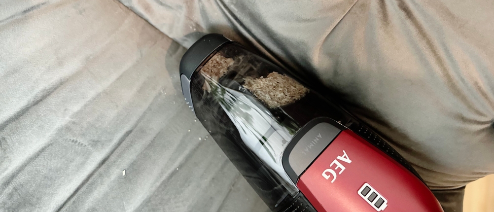 Der integrierte Handstaubsauger des AEG Ergorapido CX7-2-45AN saugt Krümel von einem hellen Sessel. Die Düse liegt flach an.